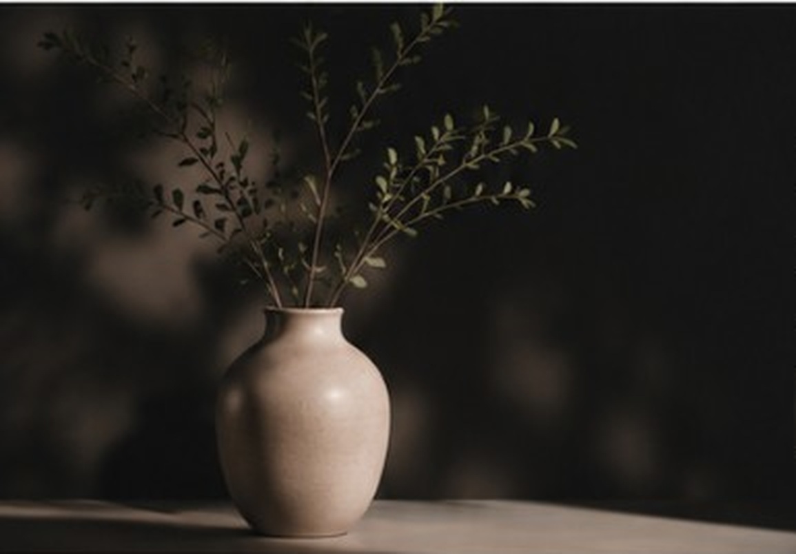 A ceramic vase with delicate greenery in warm, dramatic light.